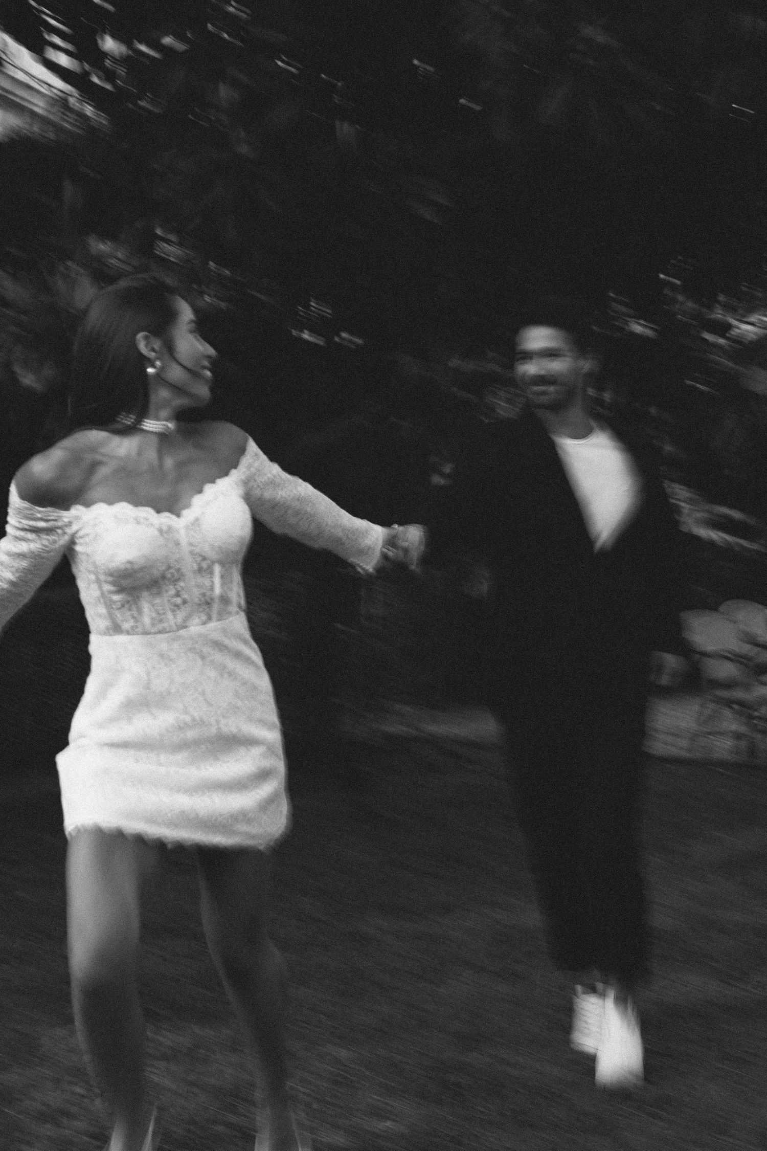 Blurry black and white motion photograph of bride and groom running in an outdoor setting.
