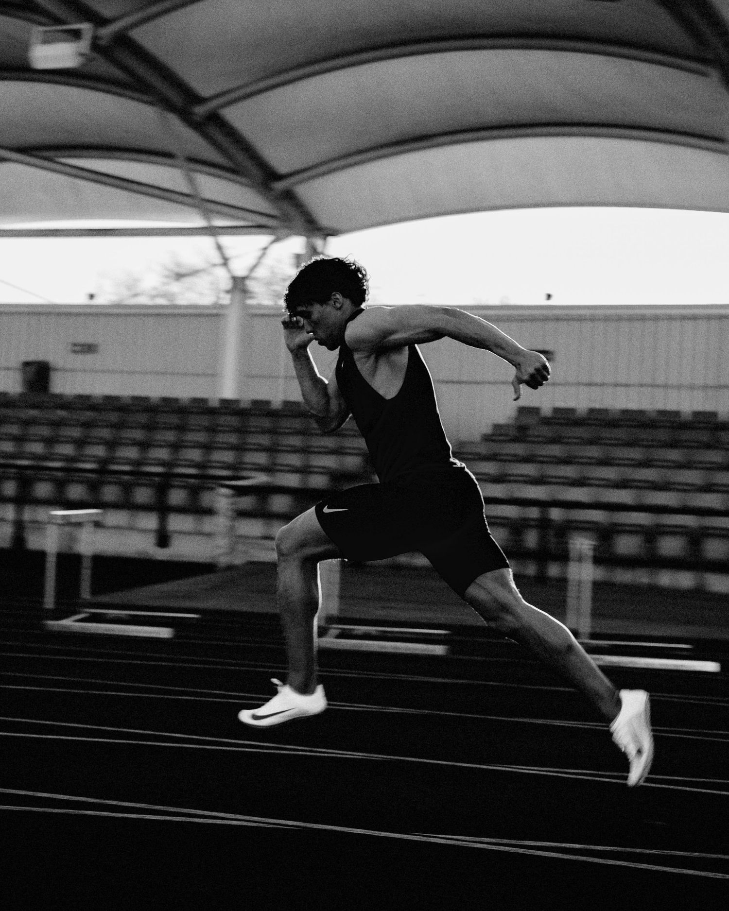 Dynamic black and white action shot of an athlete running on a track under a covered stadium.