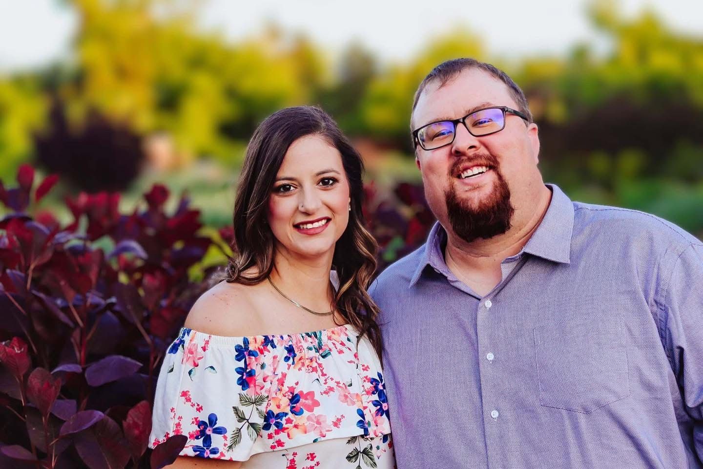 Young couple posed by flower bush.