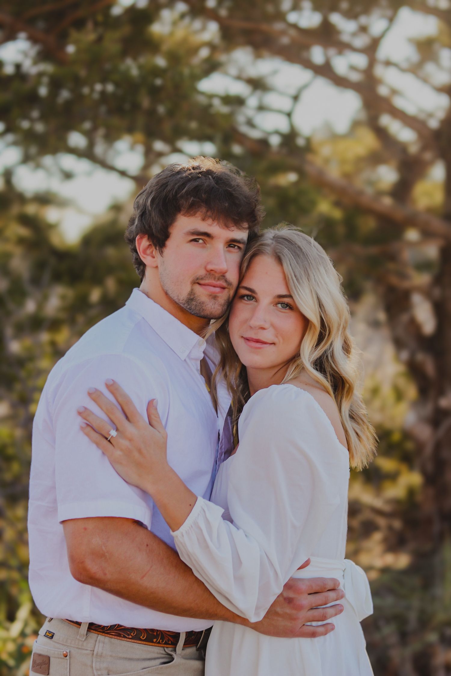 Recently engaged couple posing under a tree.