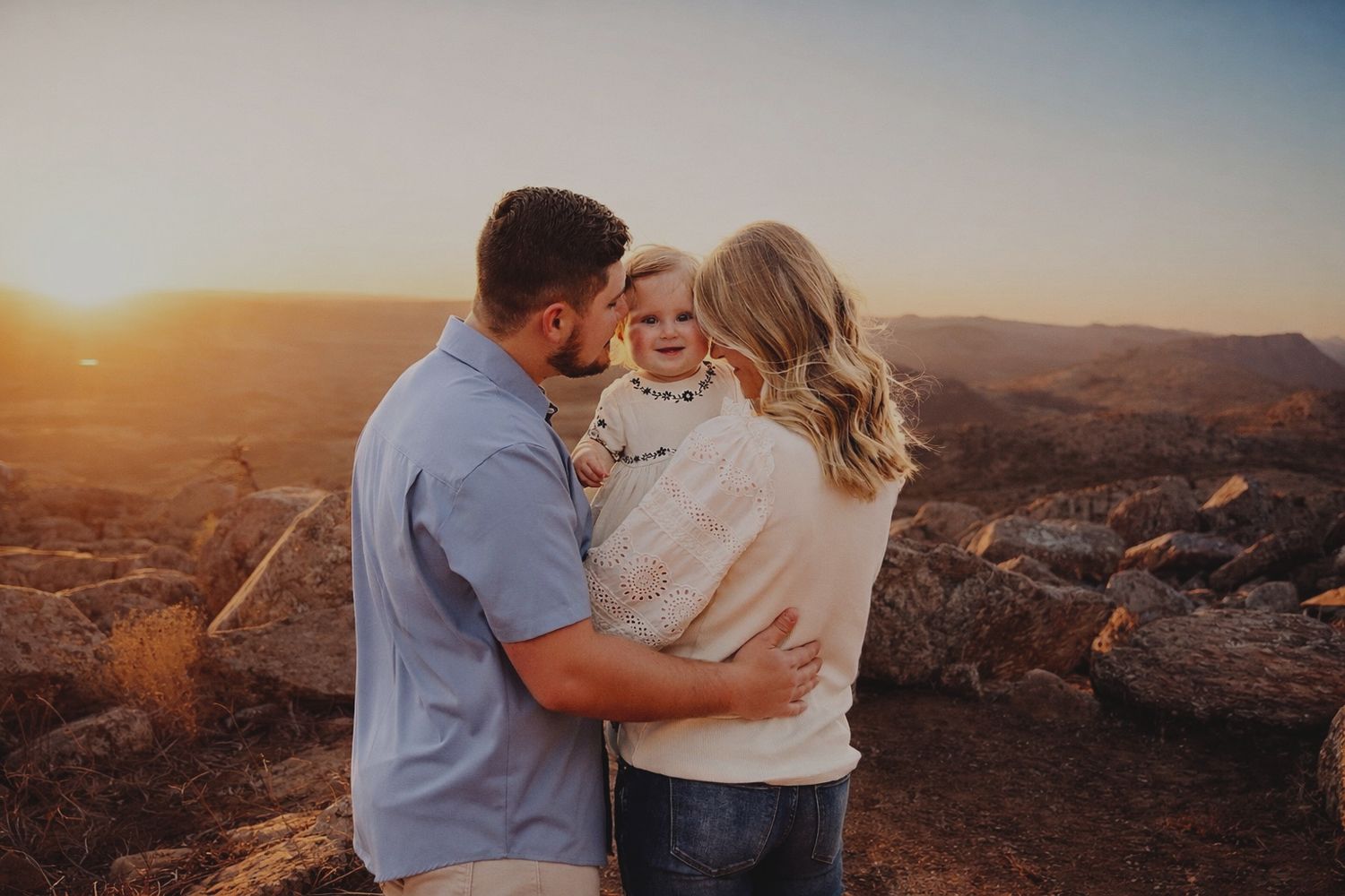 A family with a toddler posing in a field with rocks.