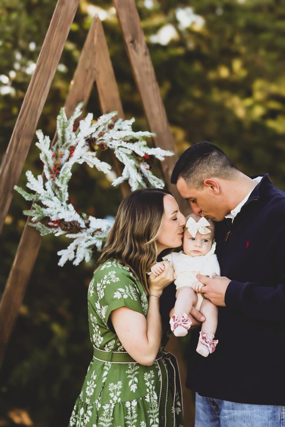Young married couple kissing baby under a wreath.