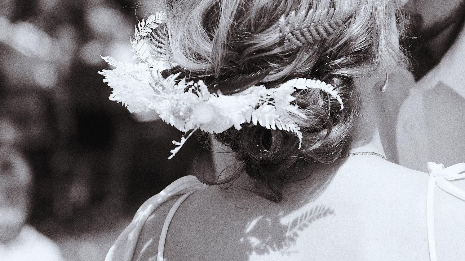 Black and white close-up of a bride's elegant updo hairstyle adorned with white floral and fern accessories.