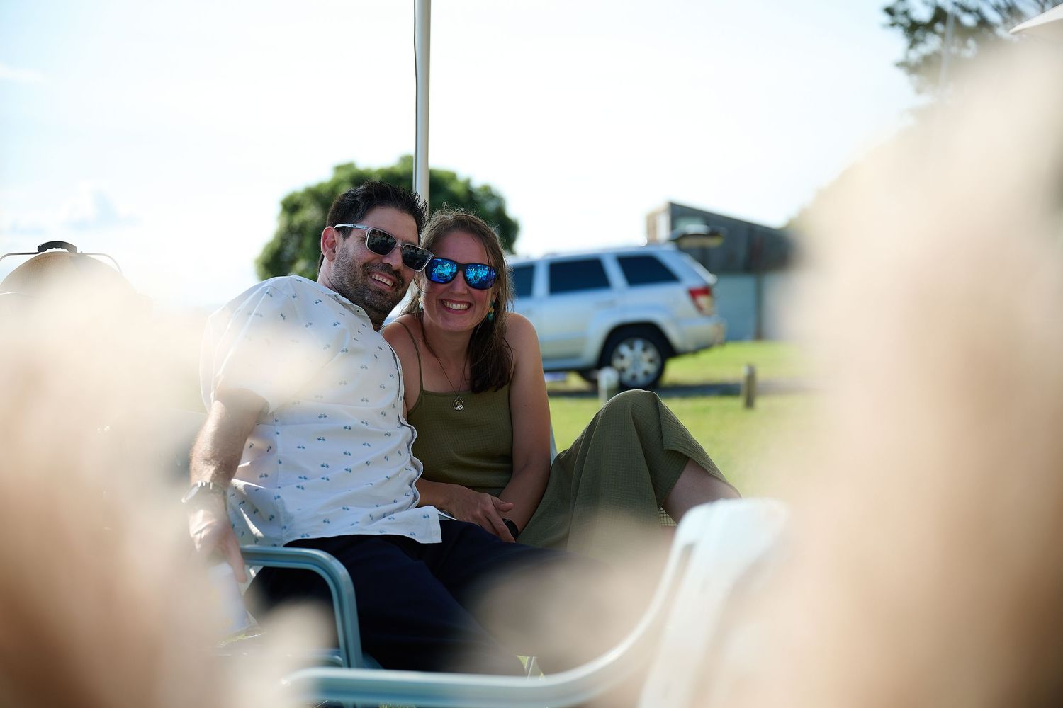 A smiling couple sitting closely together outdoors on a sunny day at a casual gathering.