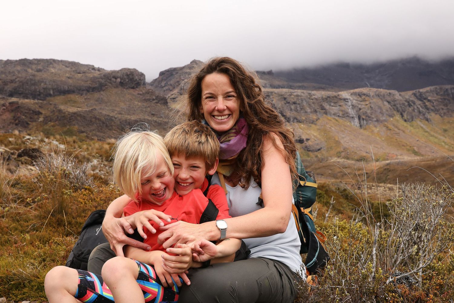 Woman with two children smiling outdoors in a mountainous landscape with misty peaks in the background.