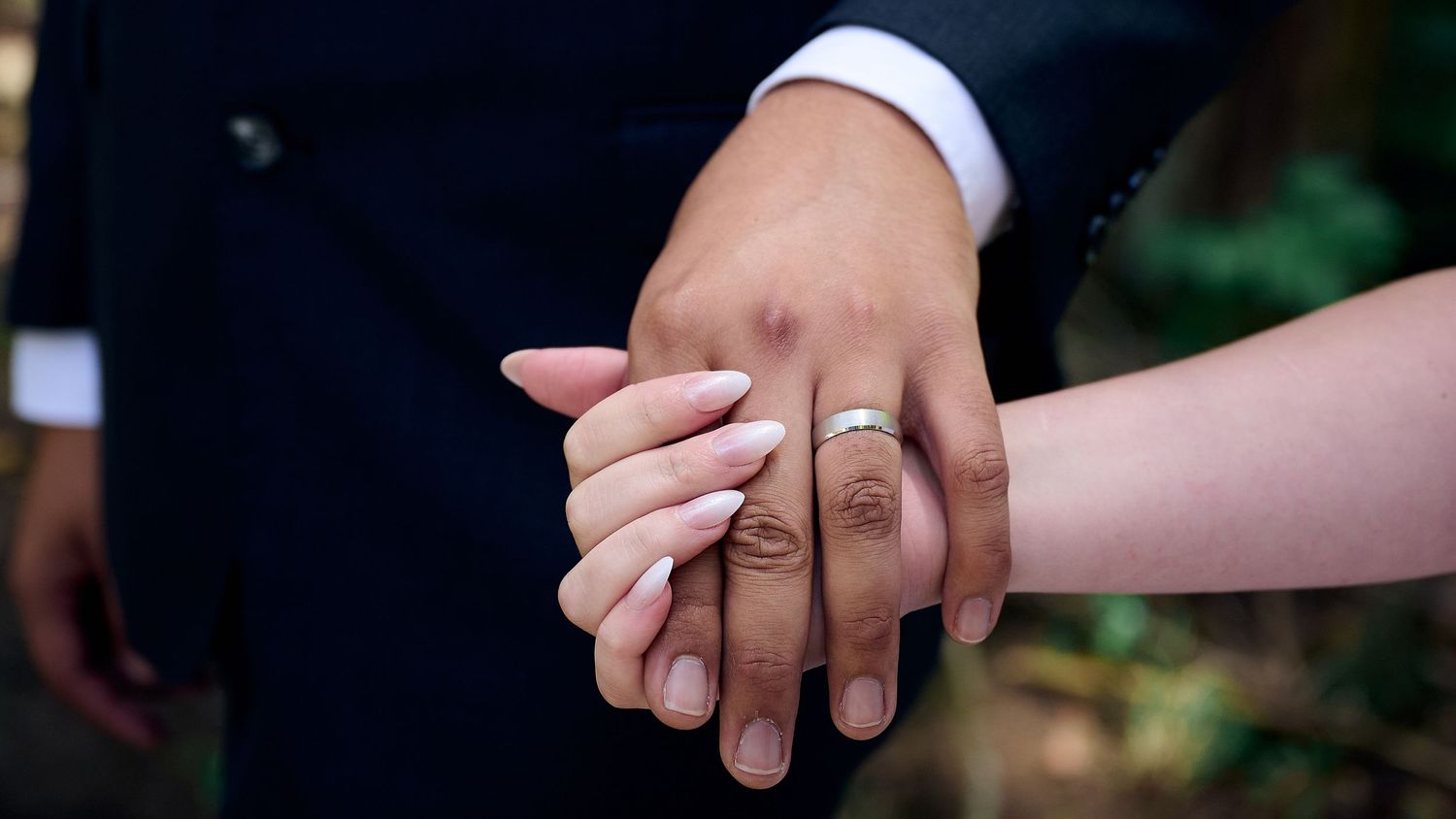 Close-up of bride and groom exchanging wedding rings with lush green foliage in the background.