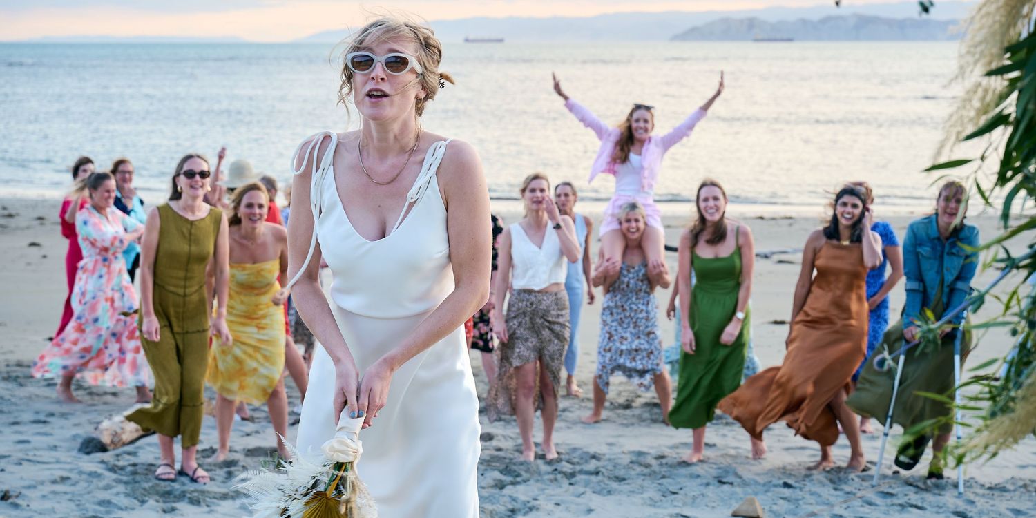 A bride in white prepares to toss her bouquet as excited guests gather behind her on the beach.