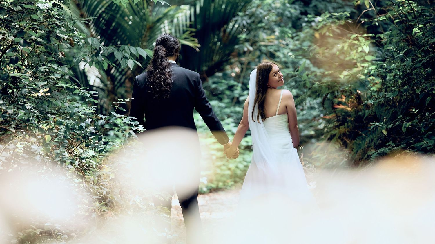 Bride and groom walking hand in hand through a lush tropical garden on their wedding day.