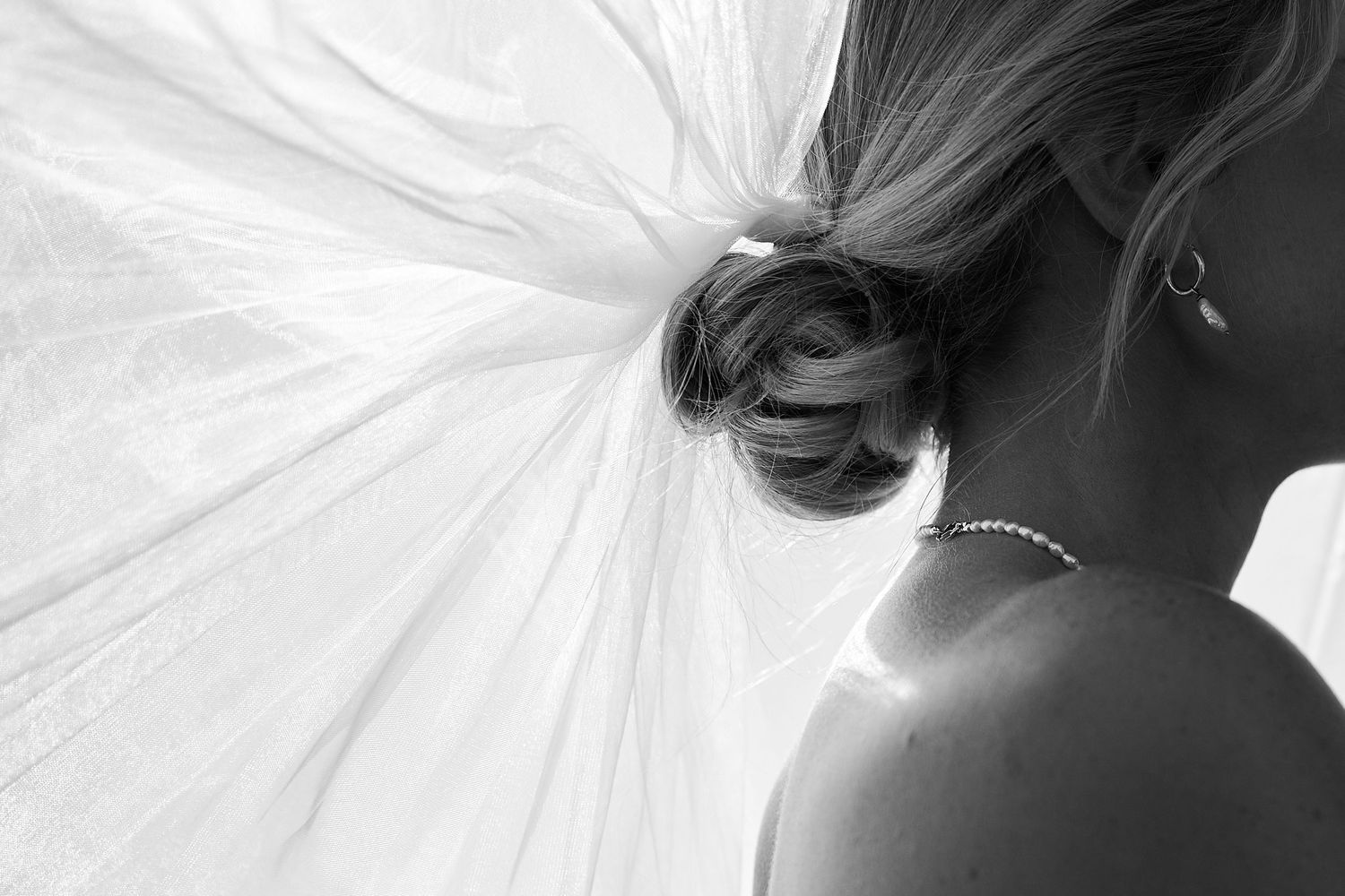 Elegant bride profile showing updo hairstyle with veil and pearl necklace in black and white.