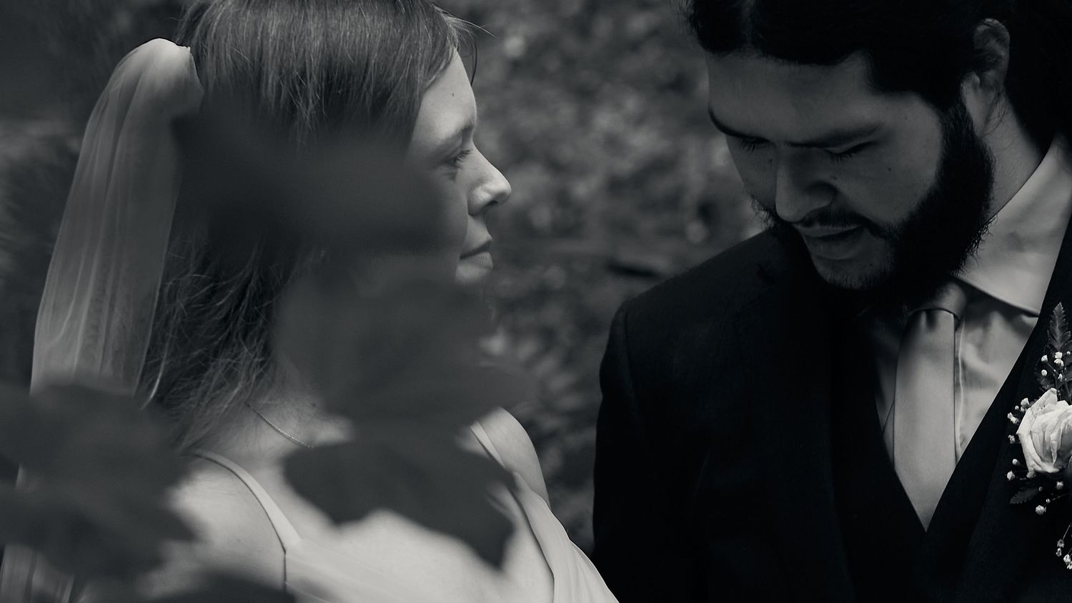 Black and white portrait of a bride and bearded groom sharing an intimate moment outdoors.