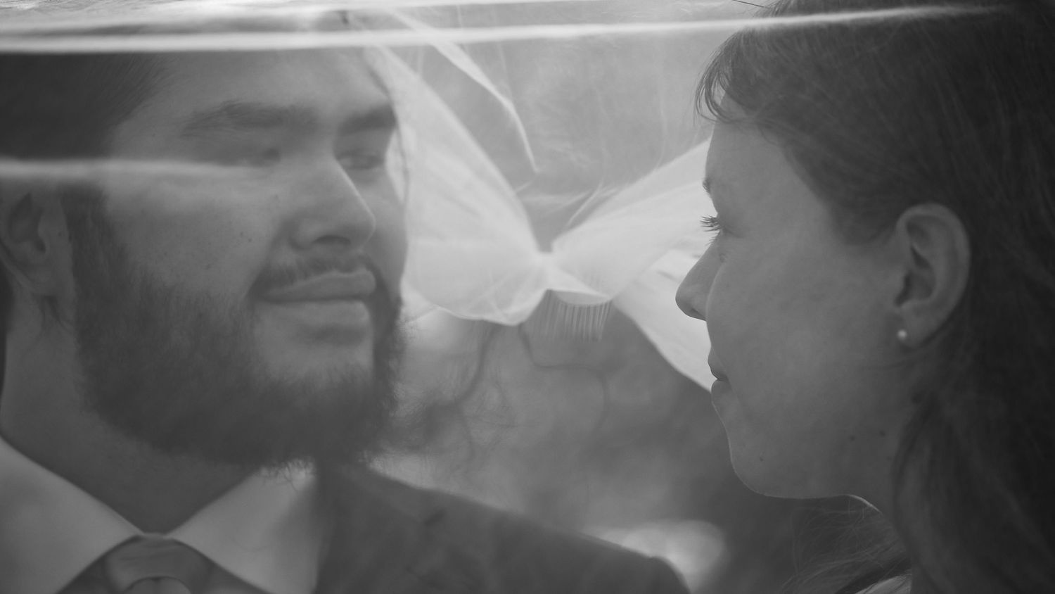 Black and white intimate portrait of bride and groom face to face beneath wedding veil.