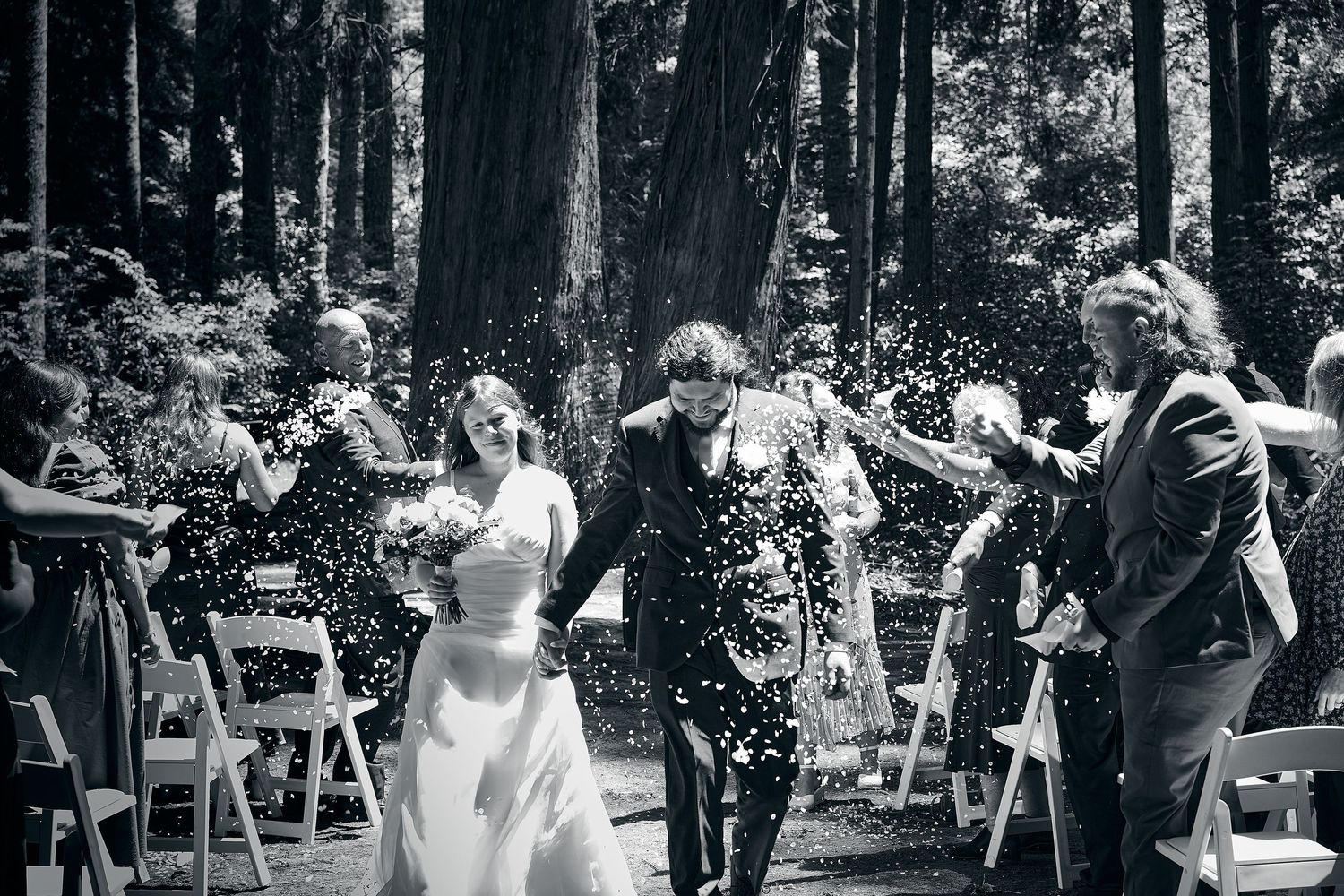 Newlyweds walking through confetti shower in black and white forest wedding photo.