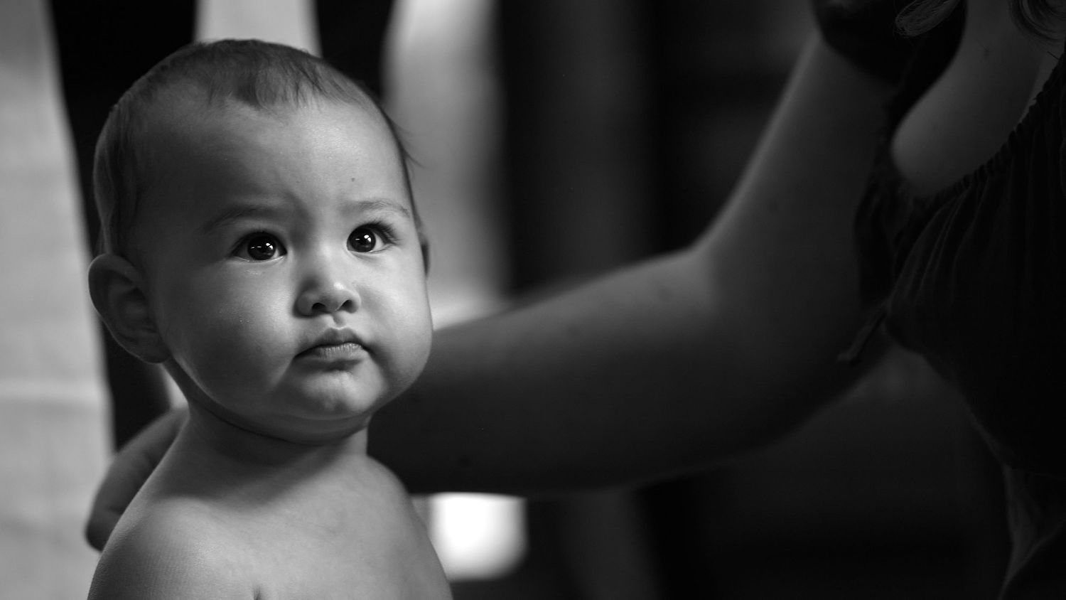 Black and white close-up portrait of a curious baby being held by an adult.