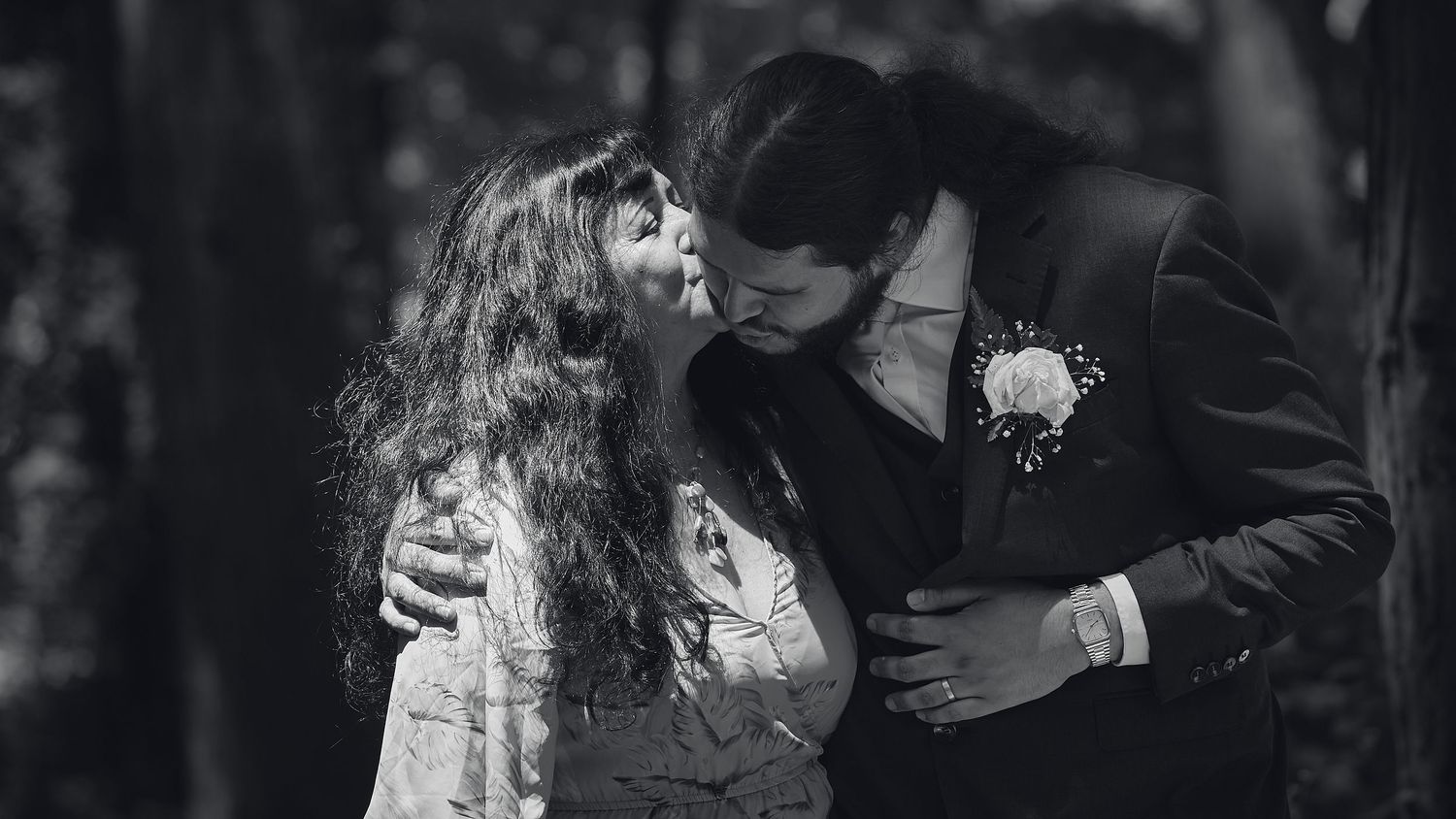 Black and white photo of couple sharing romantic kiss at forest wedding.