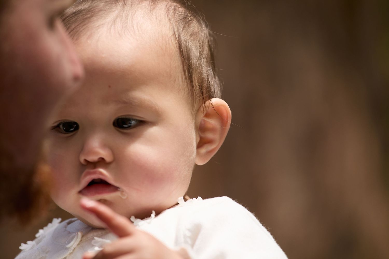 Close-up portrait of curious baby with hand near mouth in soft light.