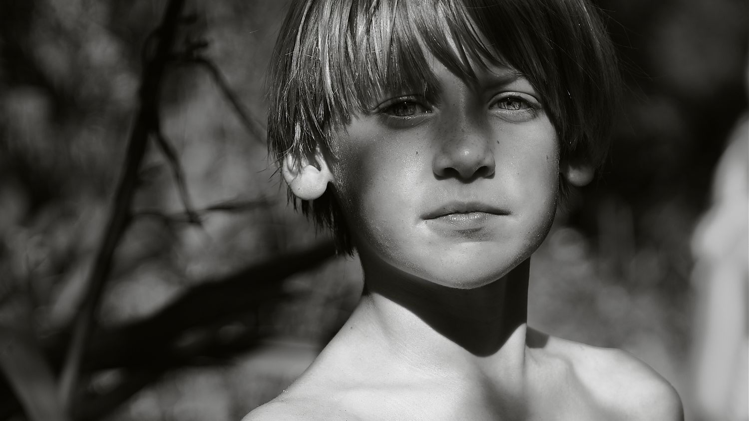 Black and white portrait of a shirtless young boy with soft natural lighting outdoors.