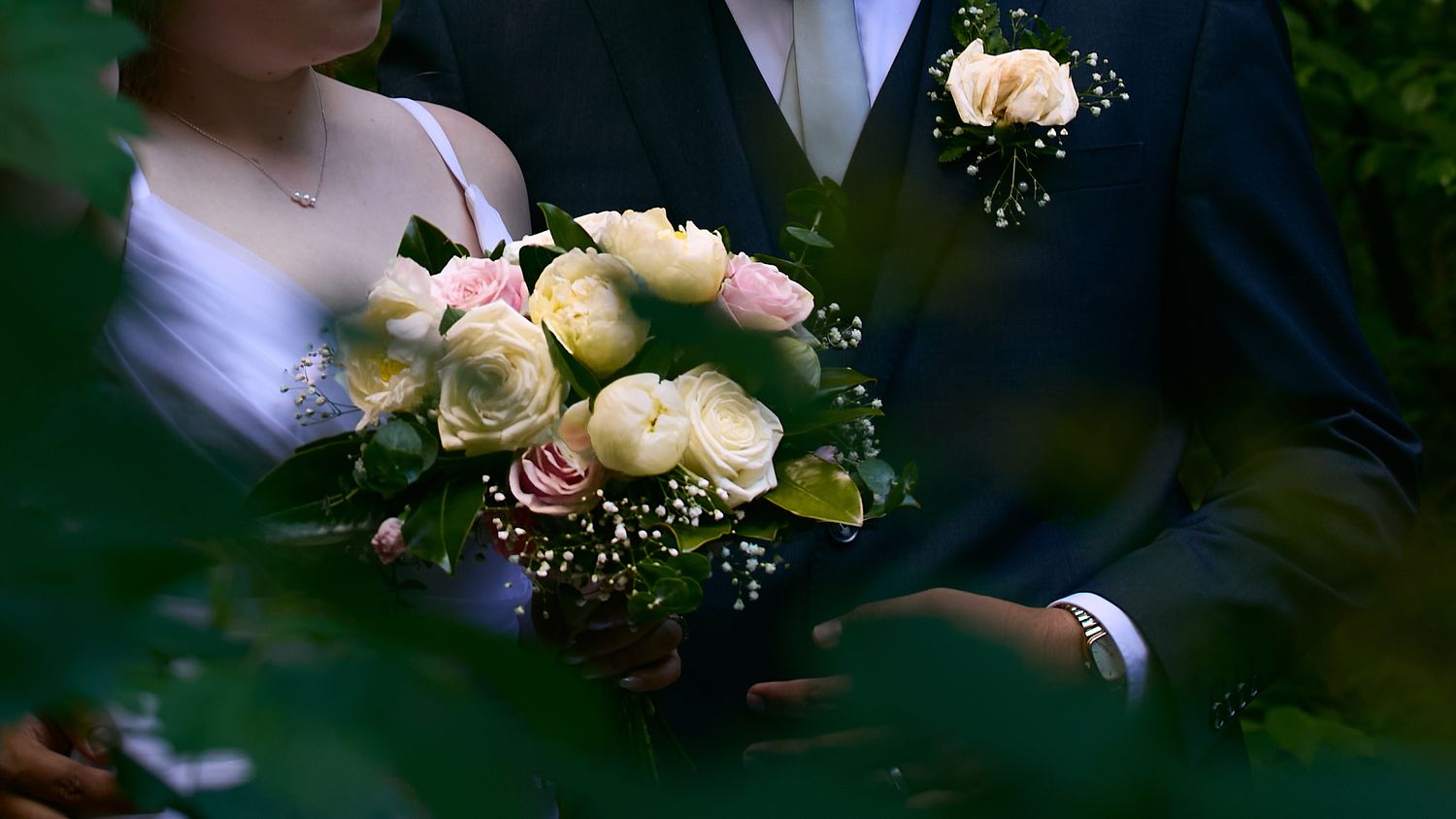 Close-up of bride and groom holding a bouquet of white and pink roses at a wedding ceremony.