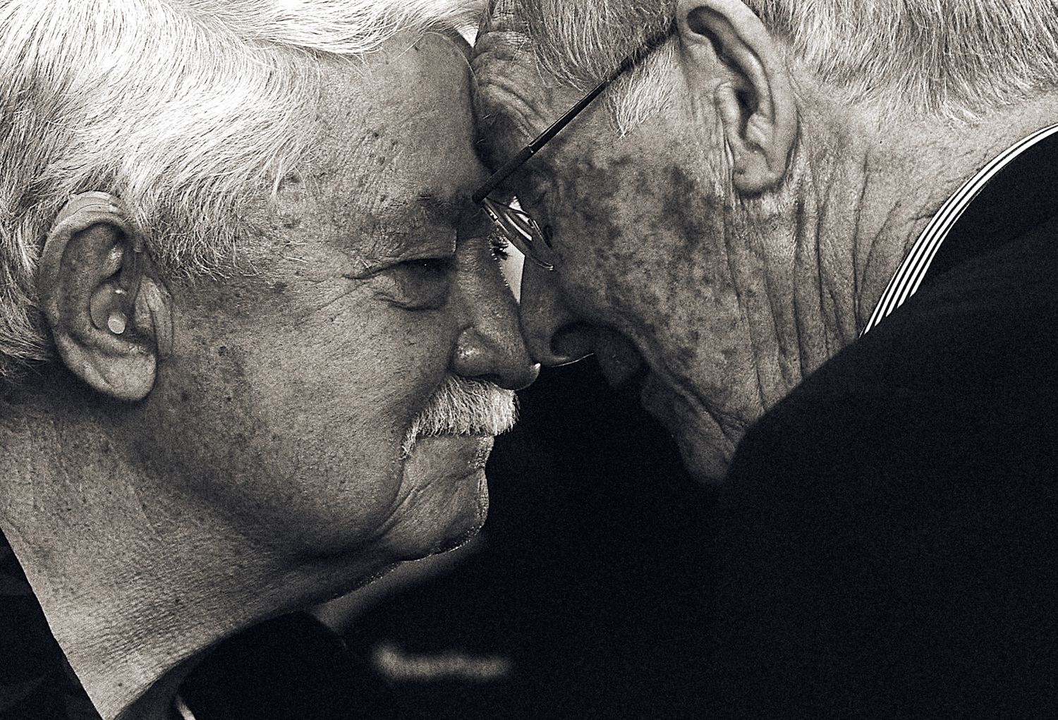Intimate black and white portrait of two elderly men sharing a close, tender moment.