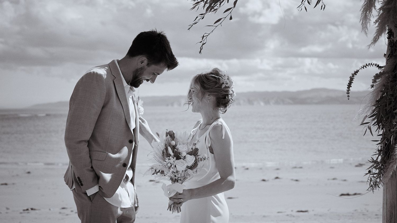 Black and white photo of a bride and groom sharing an intimate moment on a beach during their wedding ceremony.