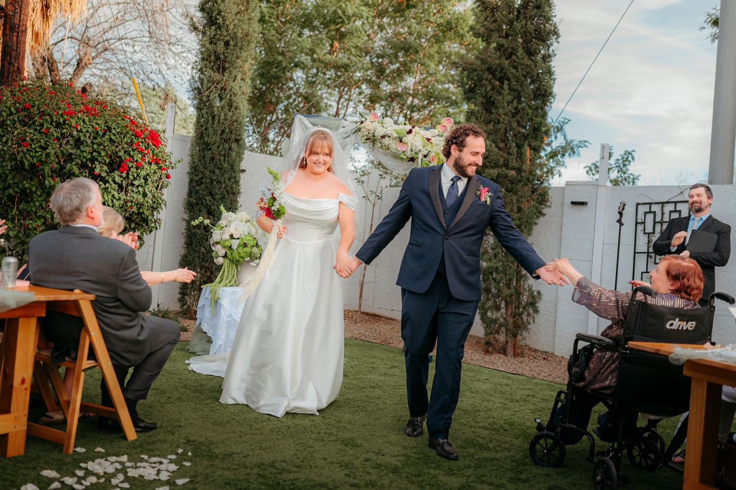 Bride and groom walking down the aisle at outdoor wedding ceremony on green lawn with floral arch.