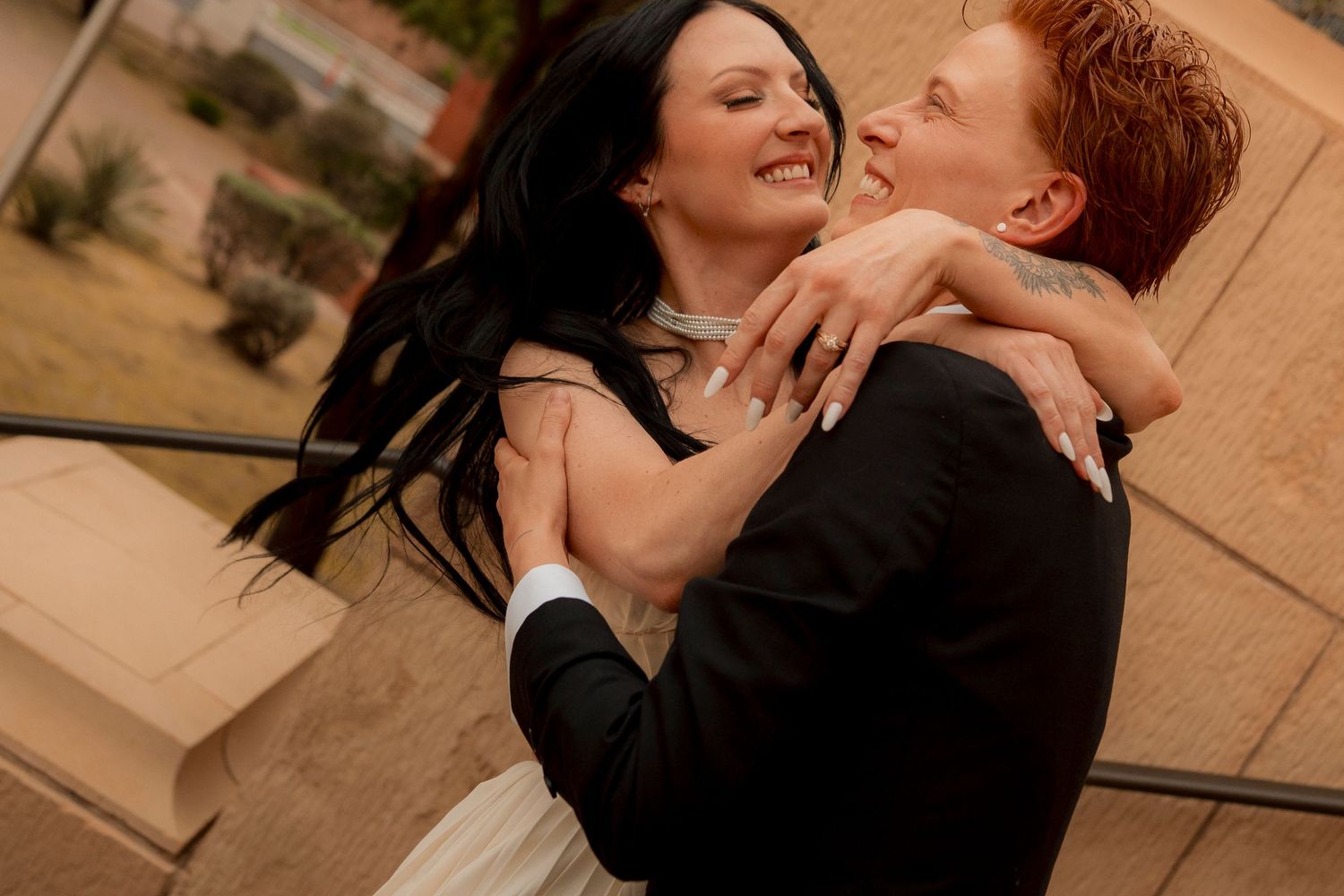 Bride and groom embracing and laughing together outdoors during their wedding day portrait session.