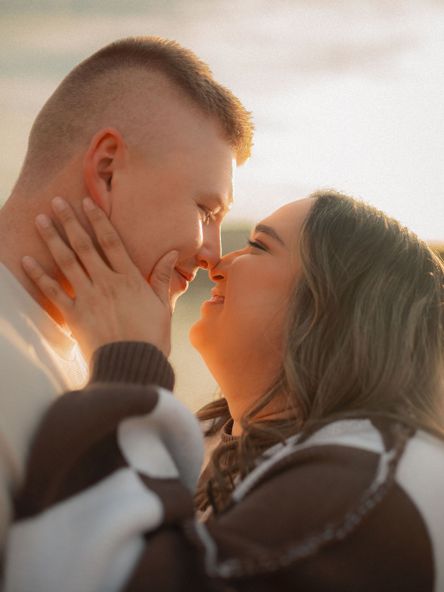 Romantic couple nearly kissing at golden sunset with warm light glowing around them.