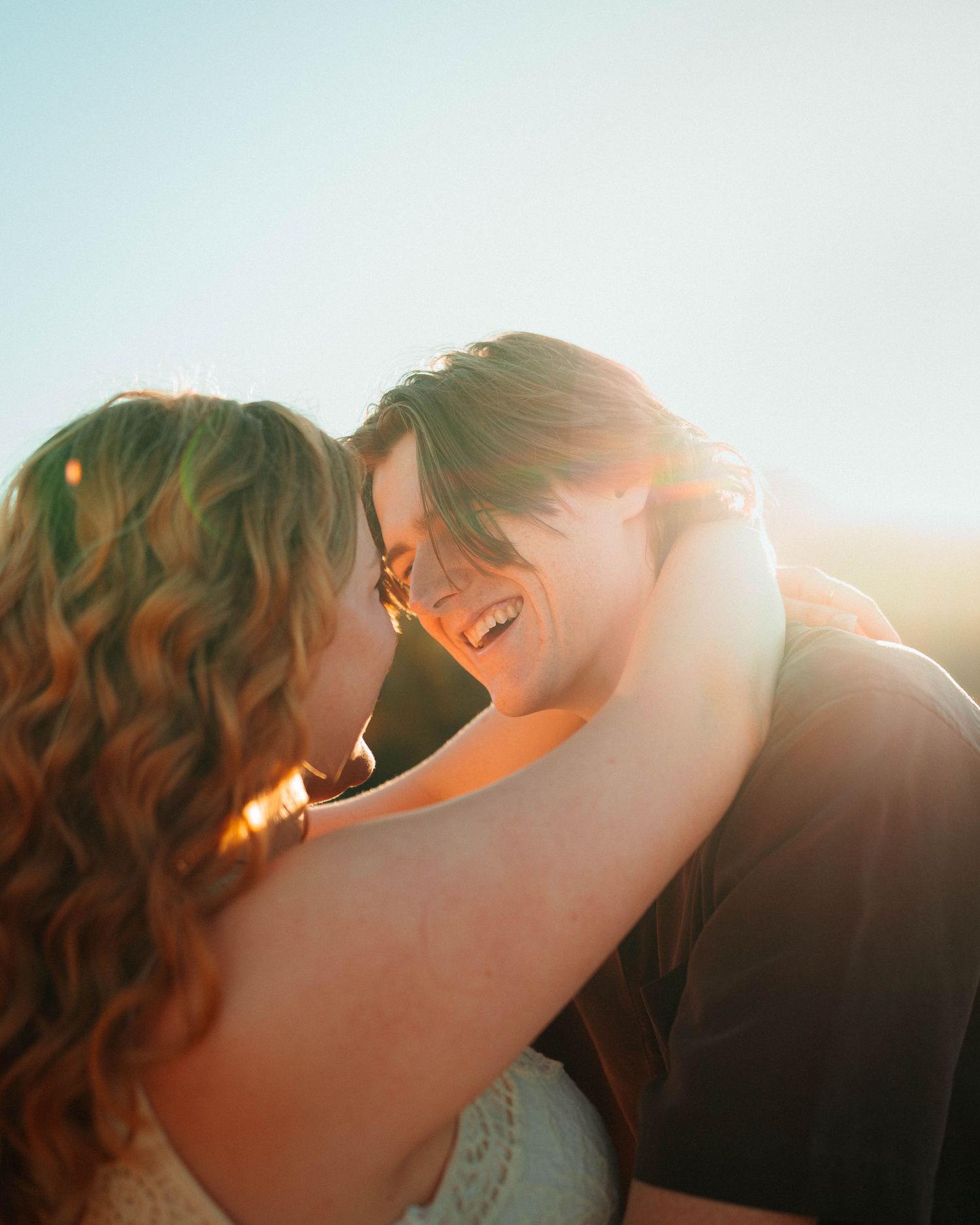 A joyful couple embraces and laughs together in warm golden sunset light, sharing a romantic moment outdoors.