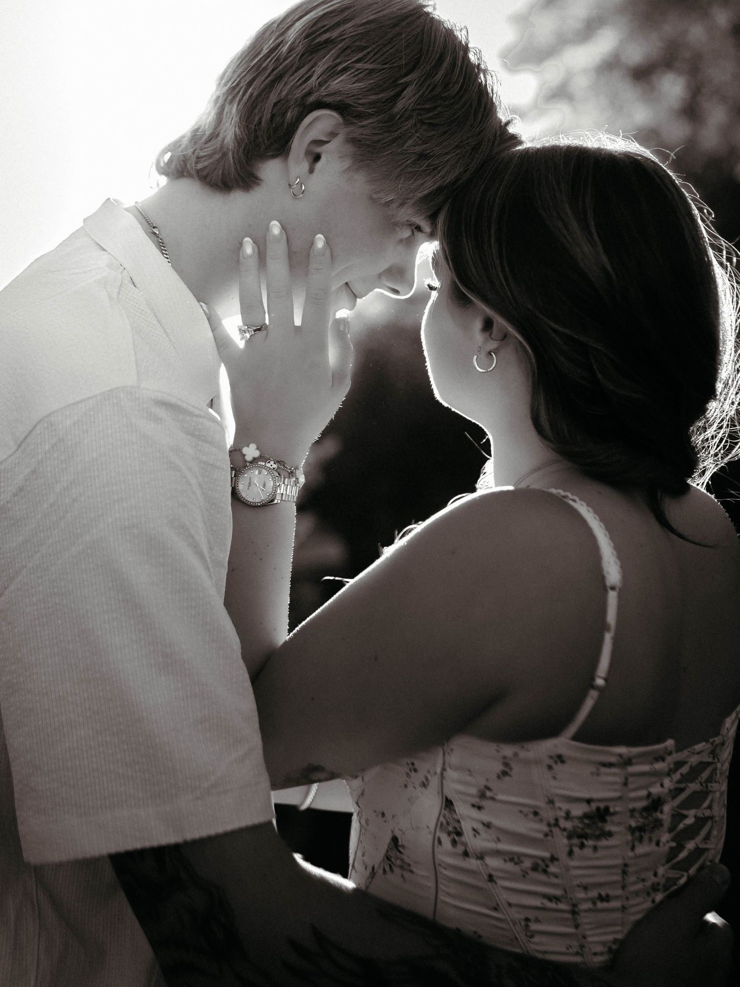 Black and white photo of a young couple sharing a romantic moment, almost kissing, woman wearing a watch and ring.