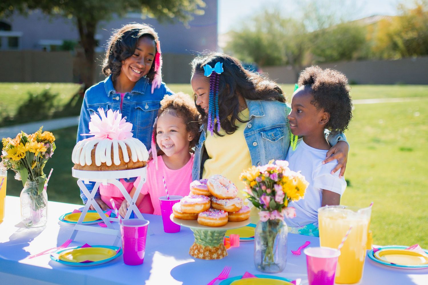 Black family with children gathered around a colorful birthday party table outdoors.