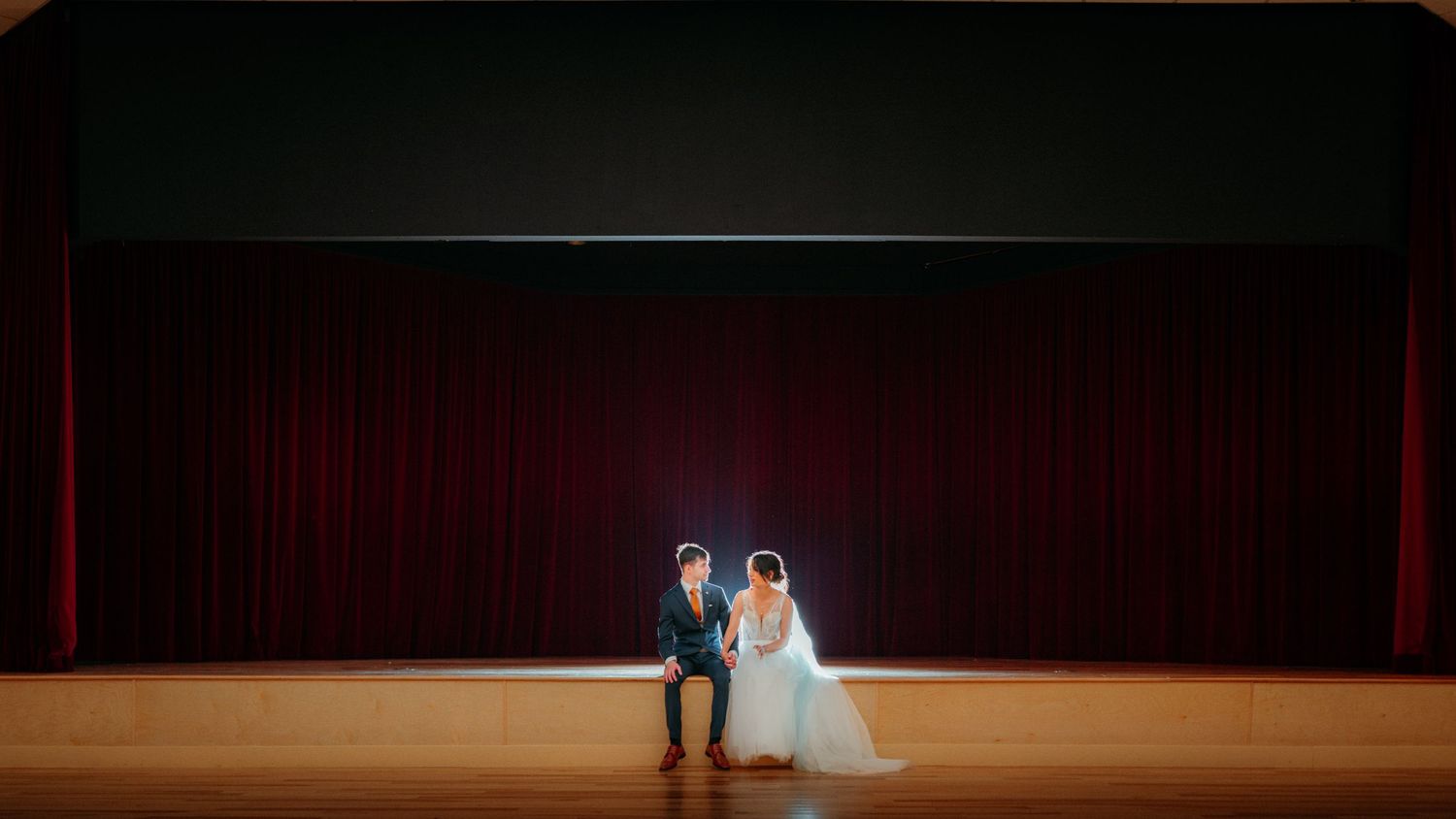 Bride and groom posing together on a stage with red curtains backdrop at their wedding ceremony.