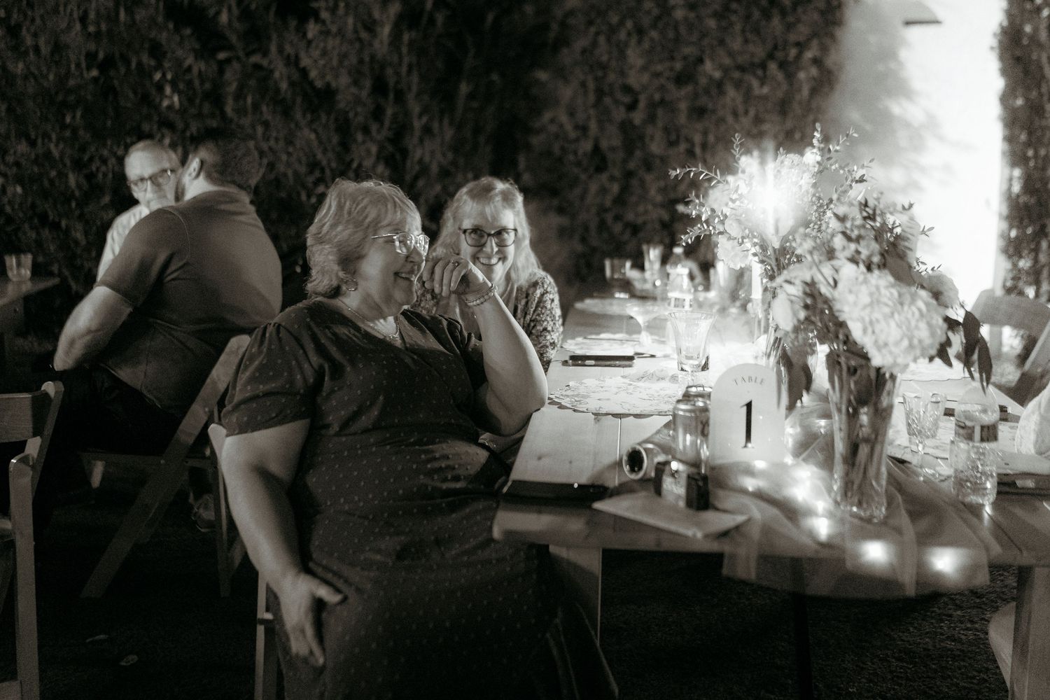 Black and white photo of wedding guests seated at candlelit outdoor reception table.