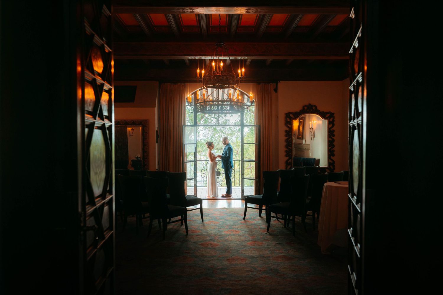 Bride and groom silhouetted in a grand arched doorway of an elegant wedding venue.