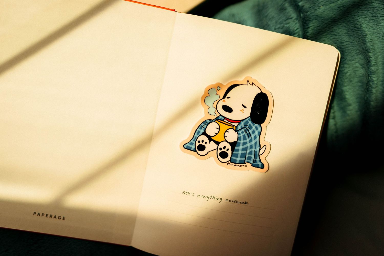 Cute cartoon dog sticker on an open notebook bathed in warm sunlight near green fabric.