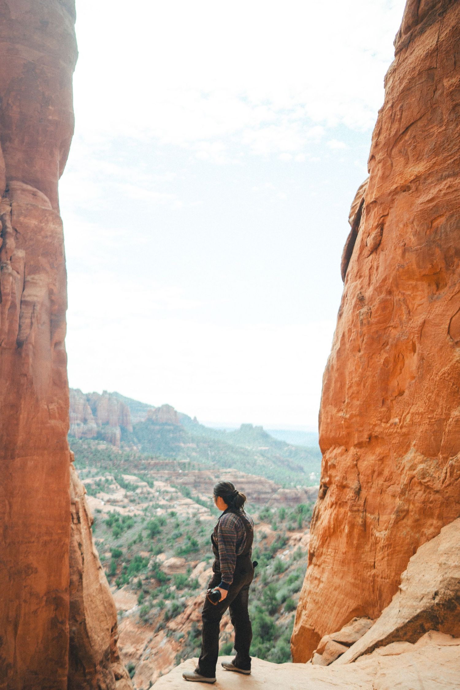 Hiker standing between towering red rock formations overlooking Sedona canyon landscape.
