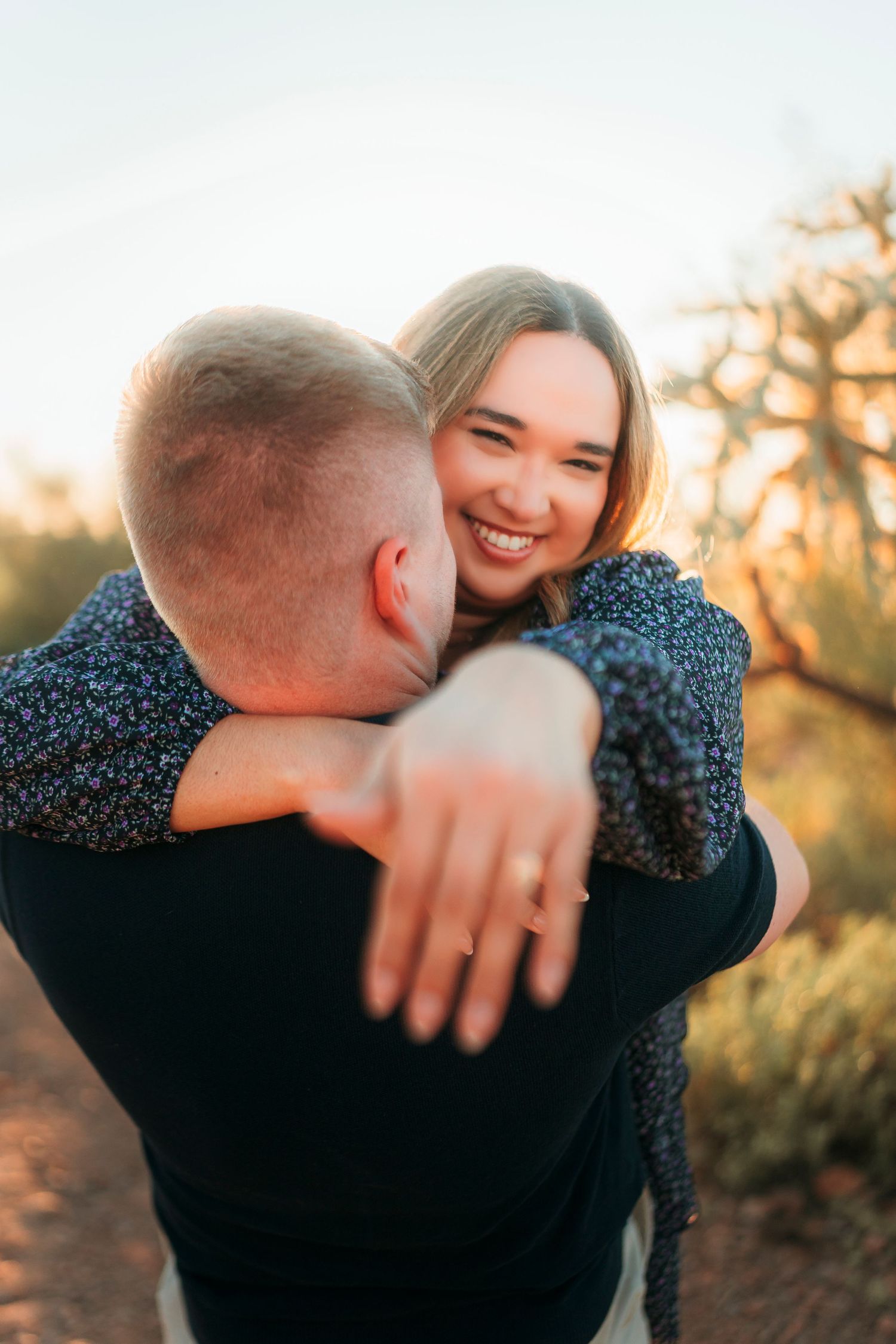 Joyful woman hugging her partner outdoors, showing off her diamond engagement ring.