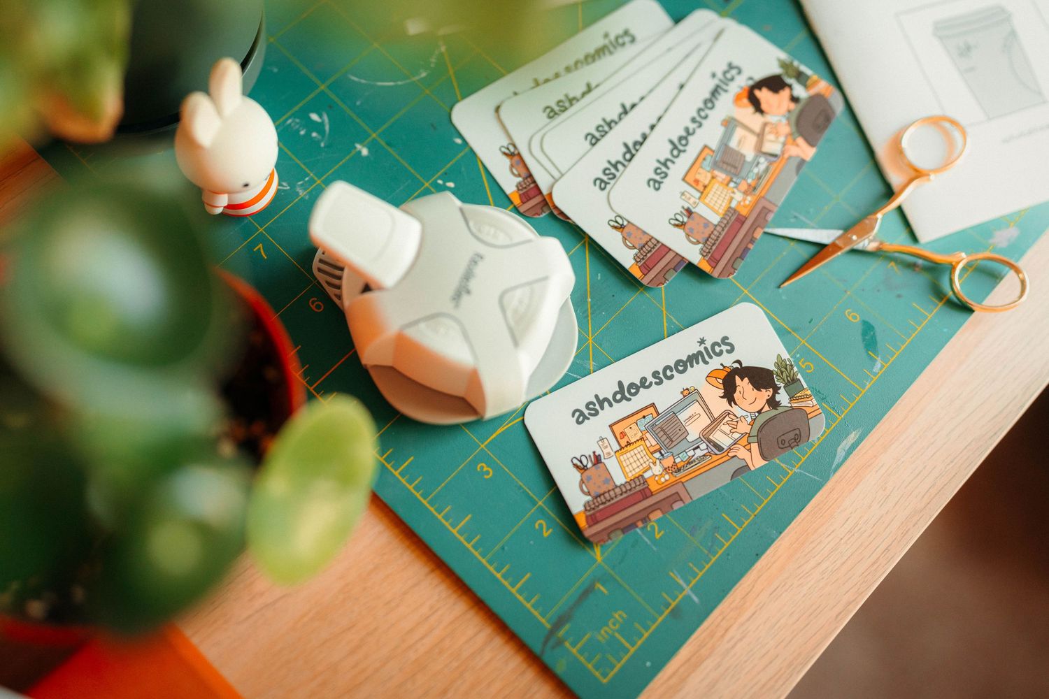 Business cards and craft supplies arranged on a green cutting mat with scissors and corner rounder.