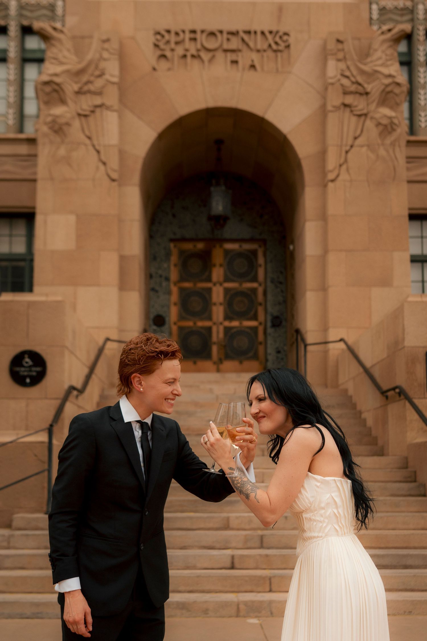 Happy couple celebrates wedding with champagne toast outside Phoenix City Hall, bride and groom smiling.