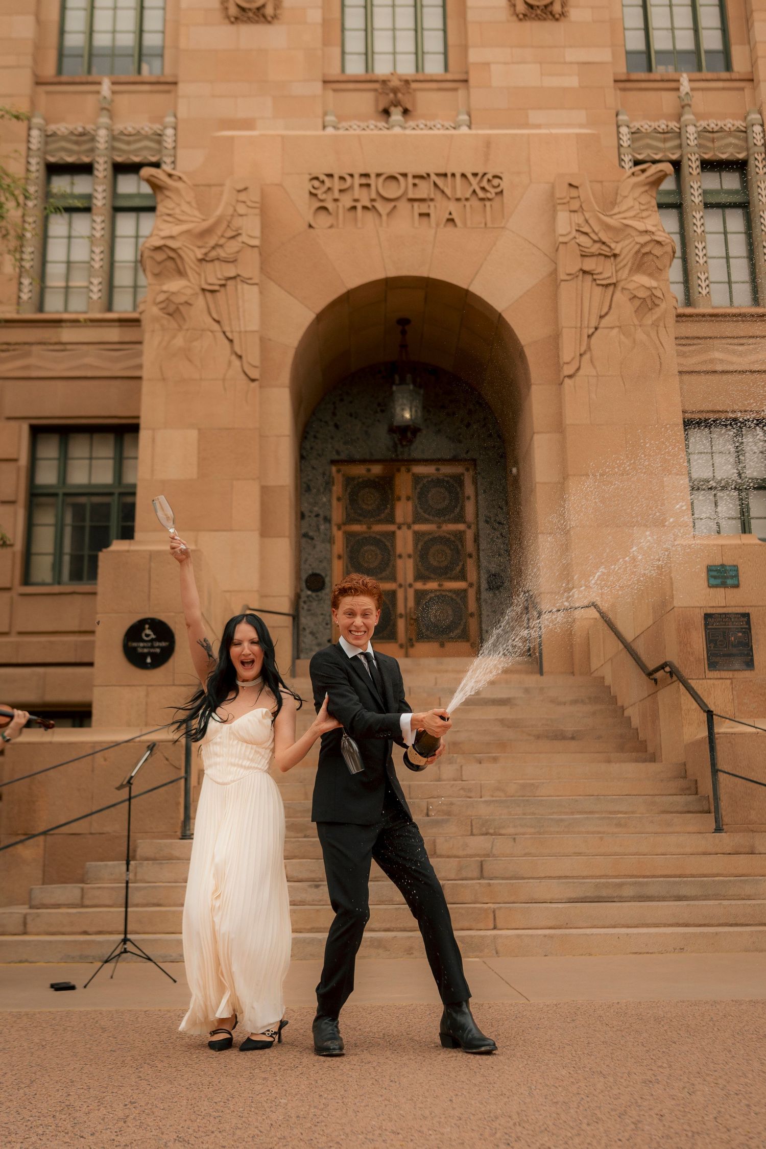 Joyful newlyweds celebrate with champagne spray outside Phoenix City Hall after wedding.