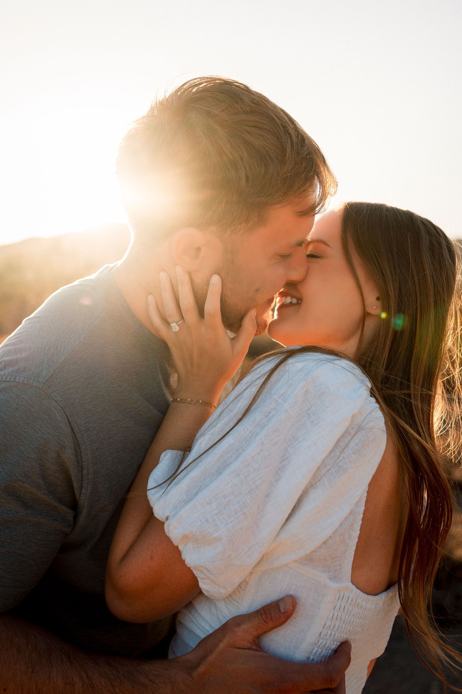 Couple sharing a passionate kiss bathed in bright golden sunlight during outdoor session.