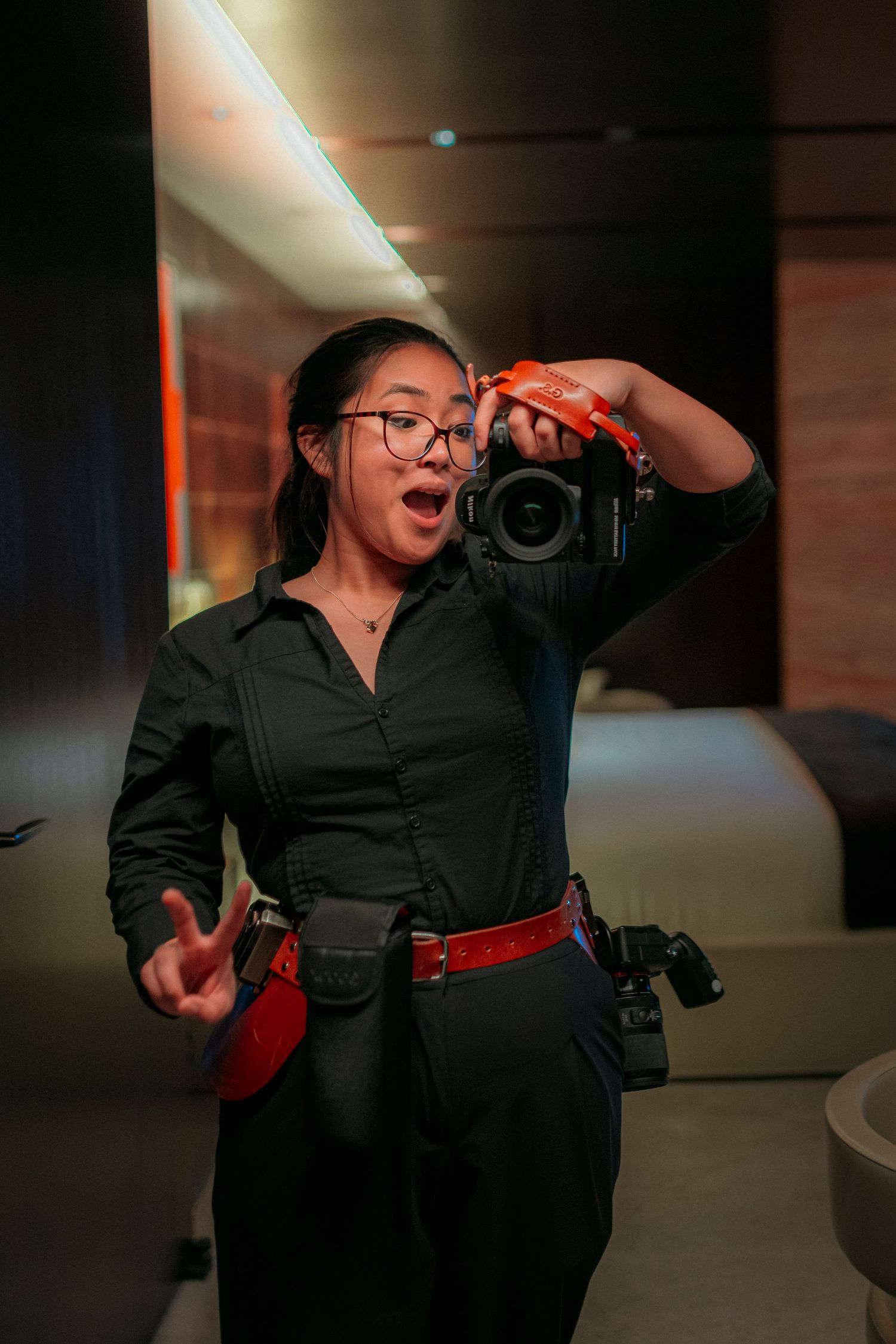 Asian female photographer posing with DSLR camera indoors with dramatic moody lighting background.