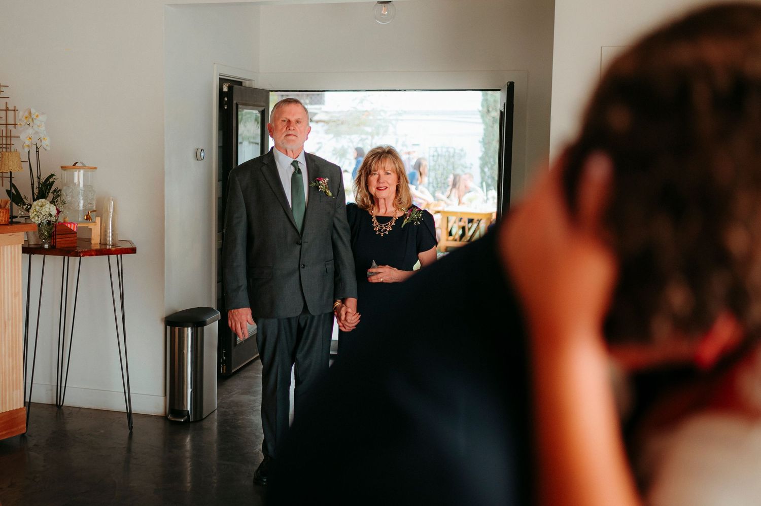 Elderly couple holding hands entering a wedding venue doorway while a photographer captures the moment.