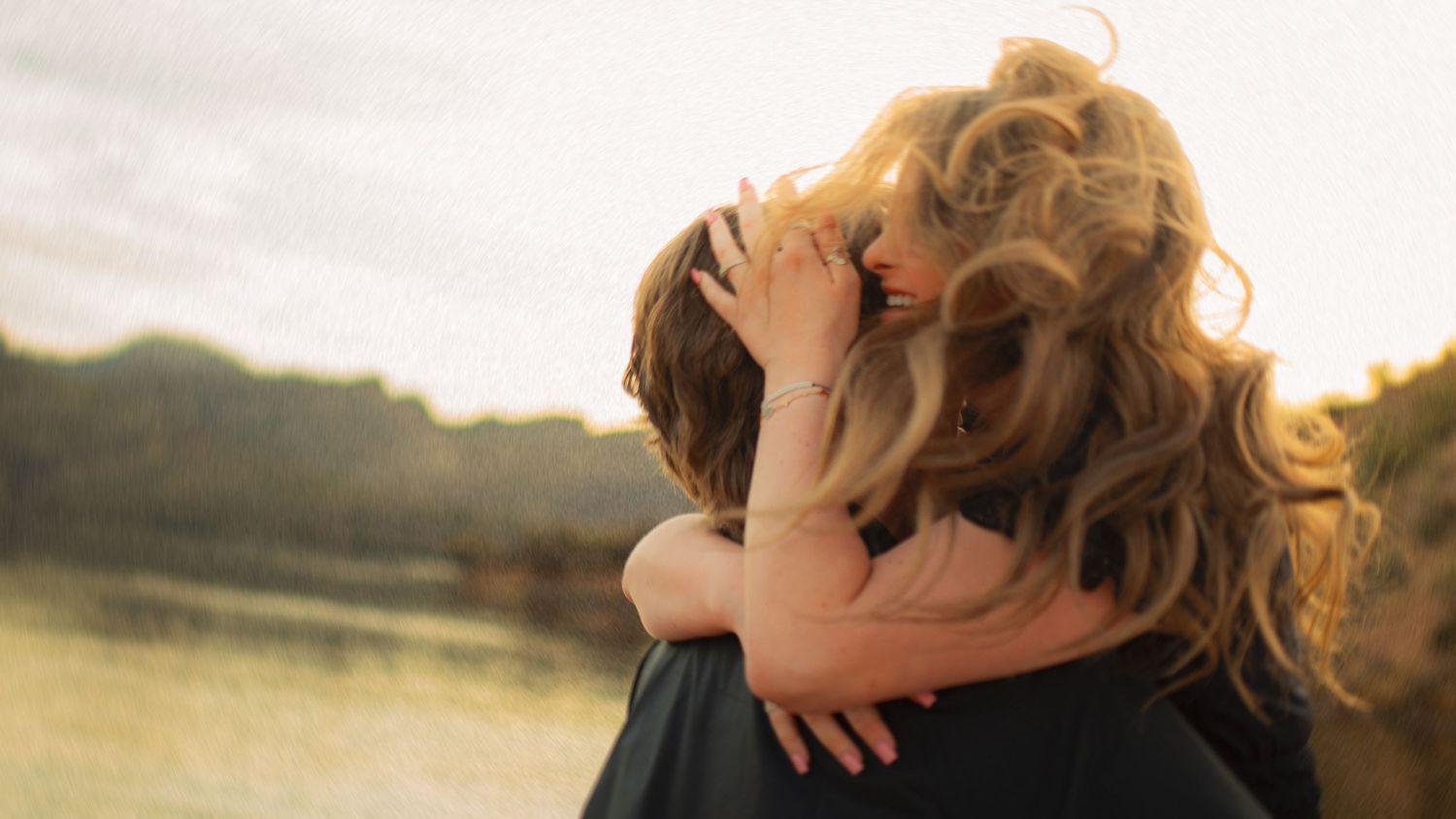 Couple sharing a warm embrace near a peaceful lake during golden hour sunset.