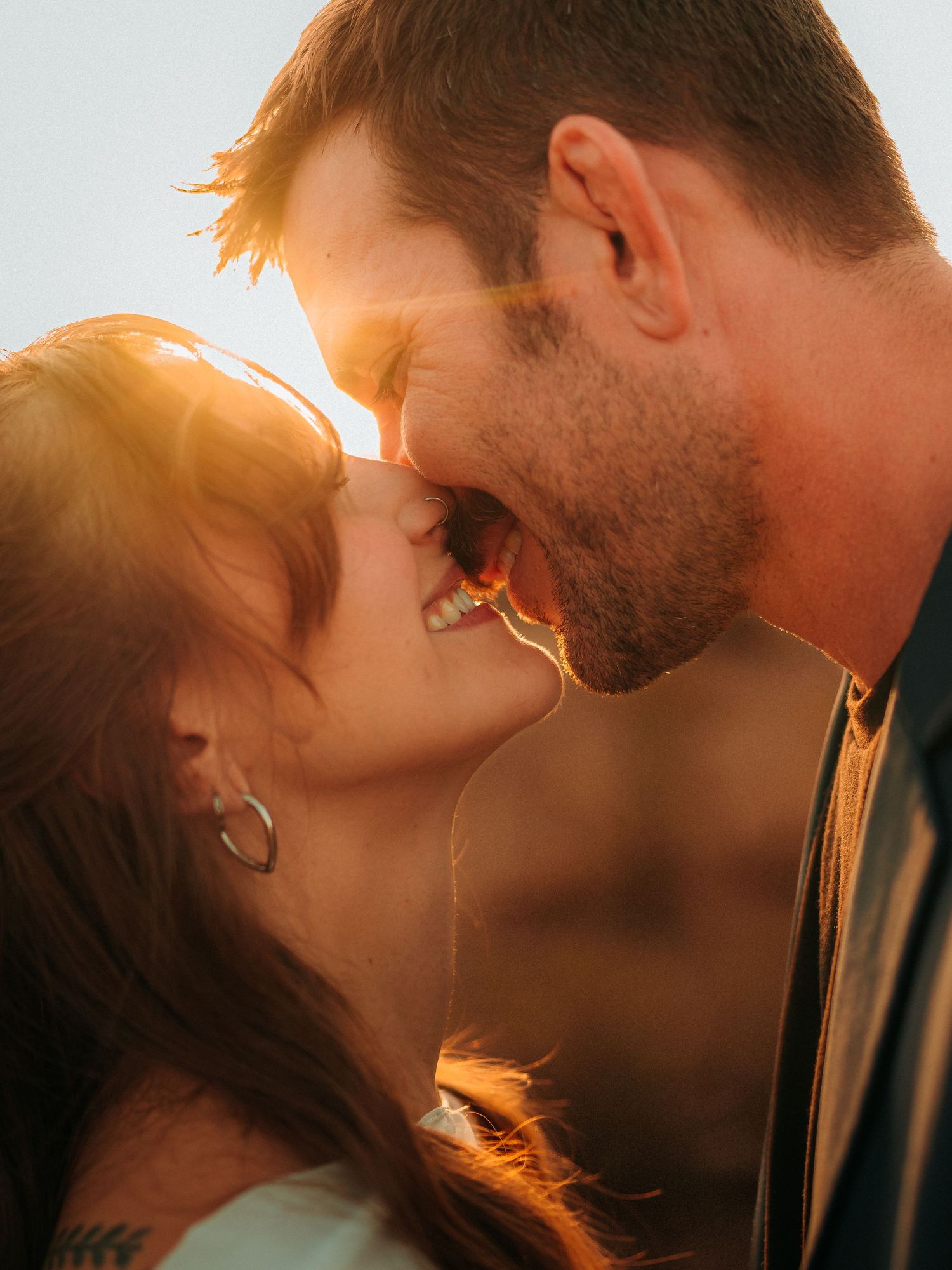 A couple shares a romantic moment, leaning in for a kiss bathed in warm golden sunset light.