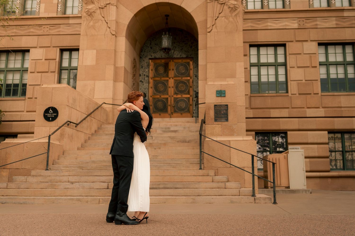 Bride and groom share a romantic embrace outside a historic stone building with ornate bronze doors.