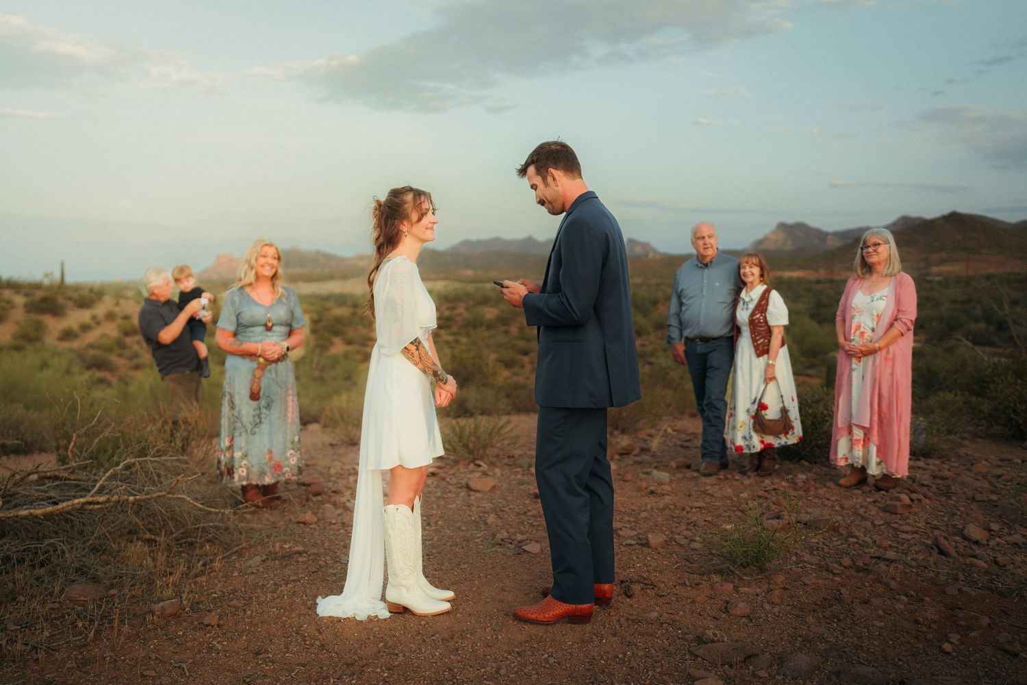 Intimate desert wedding ceremony at sunset with couple exchanging vows surrounded by small group of family in Arizona landscape.