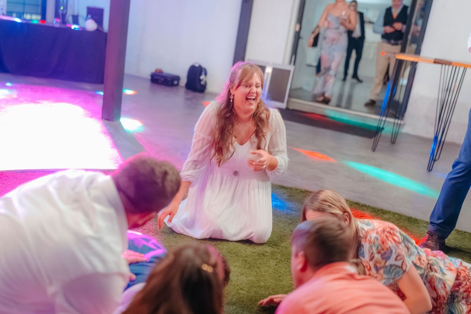 Wedding guests laughing and playing on colorful dance floor at lively reception.