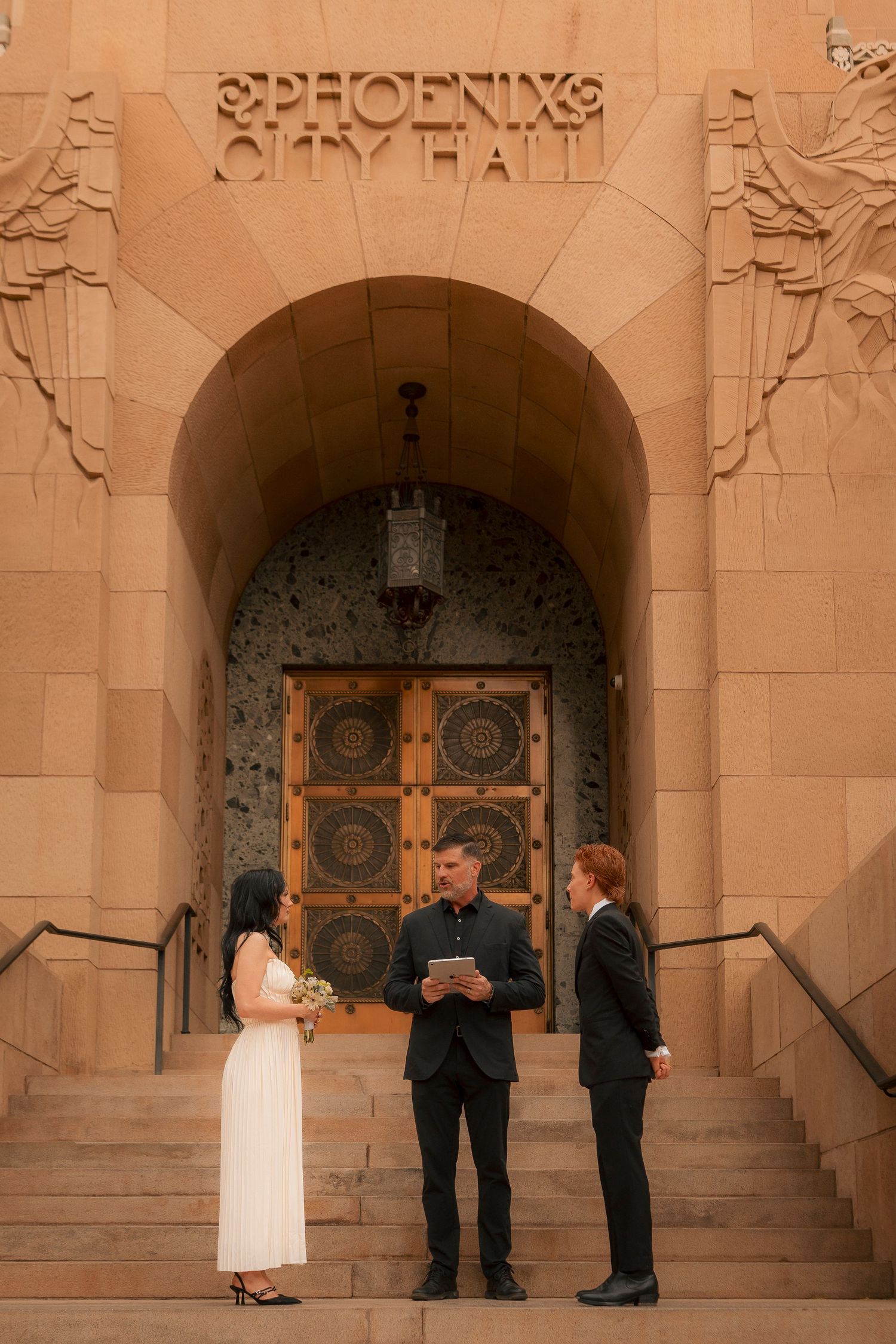 Couple exchanges vows with officiant at Phoenix City Hall entrance during an intimate outdoor wedding ceremony.