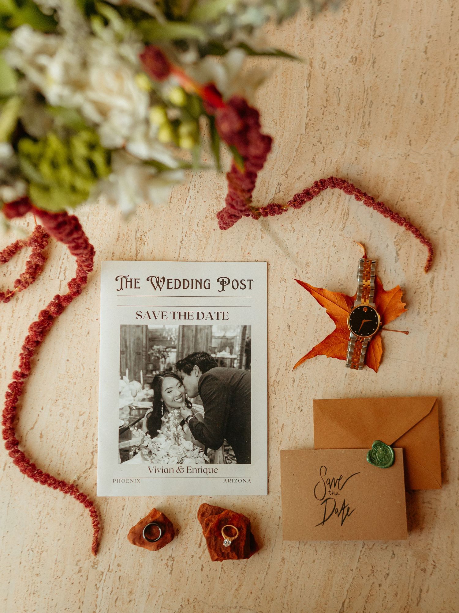 Elegant wedding save the date flat lay with rings, watch, envelope, and floral accents on neutral background.