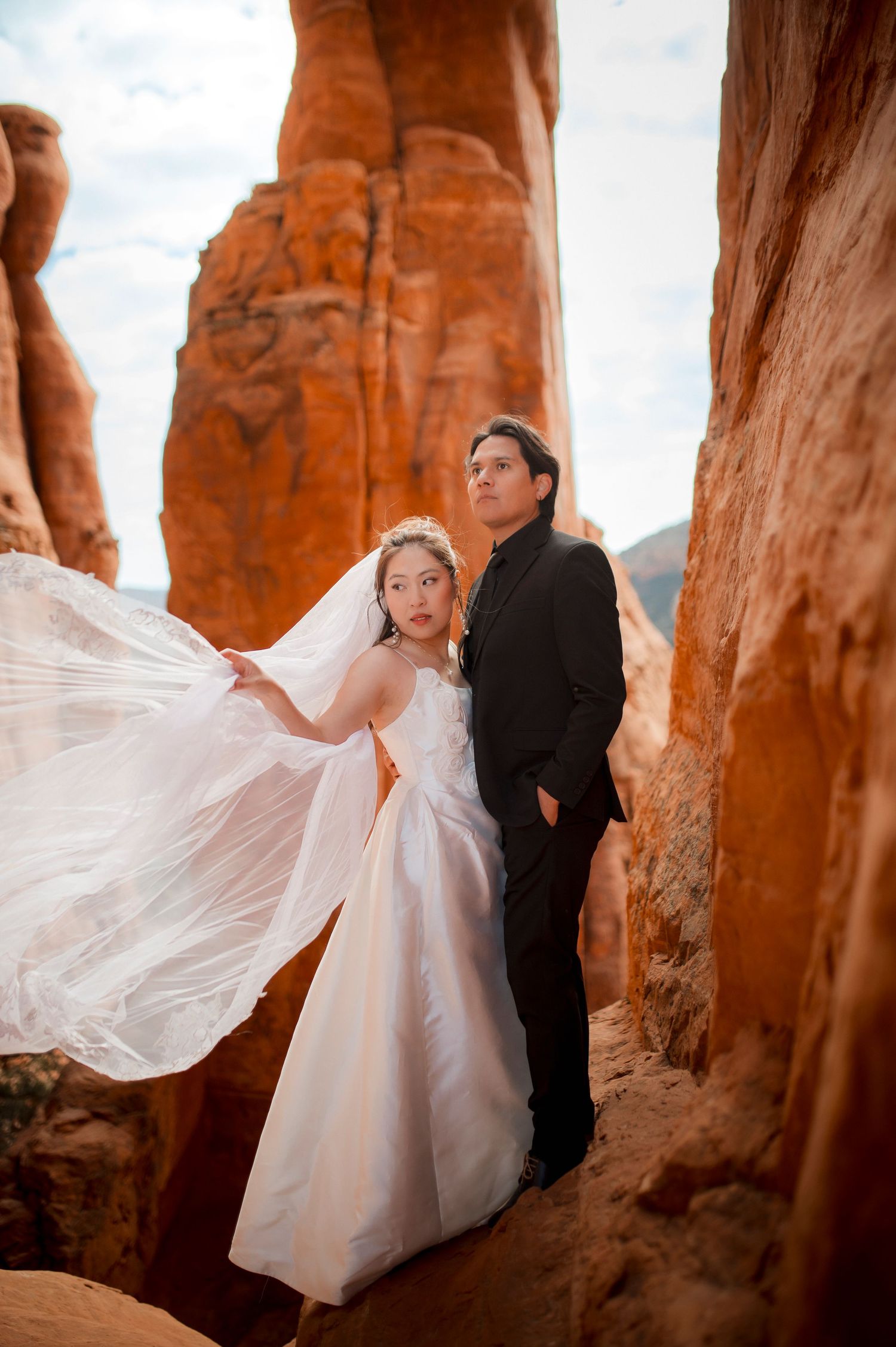 Bride and groom posing dramatically among towering red rock formations in Sedona, Arizona.