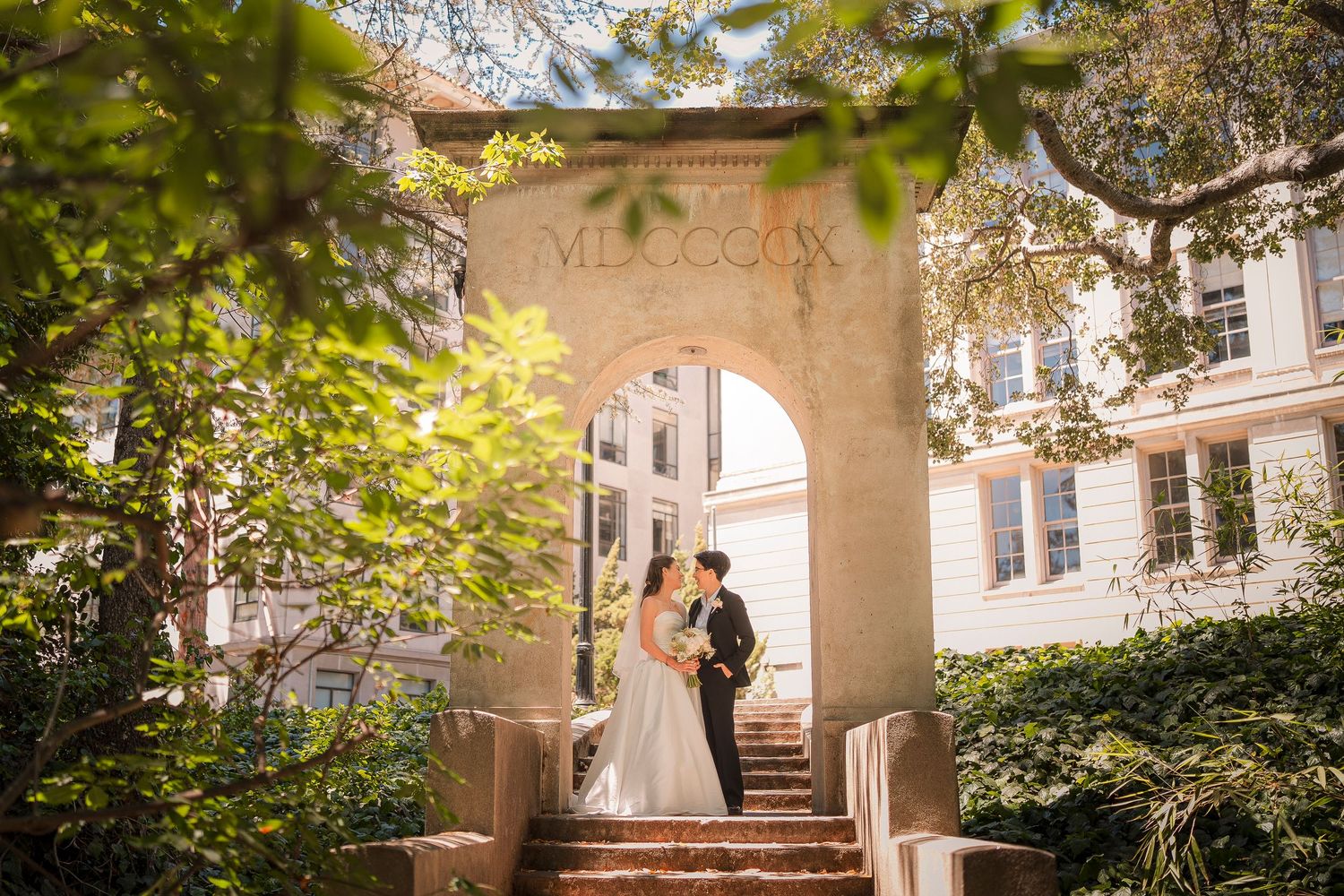 Bride and groom sharing a romantic moment under a stone arch surrounded by lush greenery.